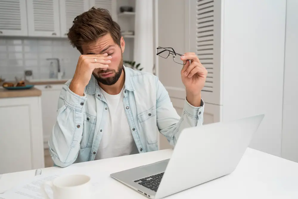 How to Adjust Screen Settings to Ease Your Eyes - This photo shows a man rubbing his eyes, attempting to relieve eye strain after working with his laptop.