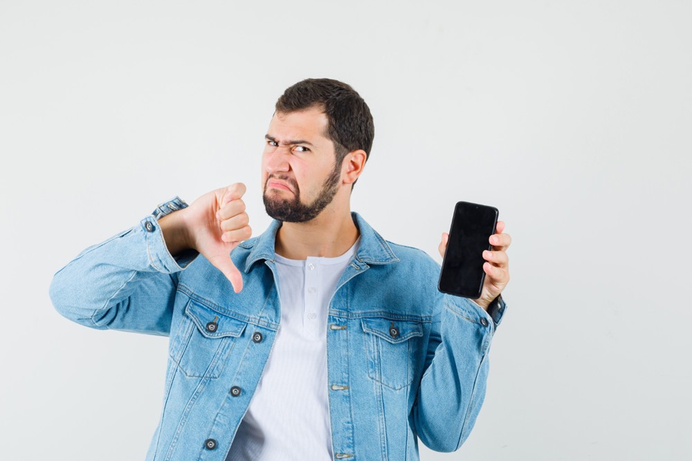 Reasons Not to Buy The iPhone 5 - This photo shows a displeased man giving a thumb down while holding a smartphone.