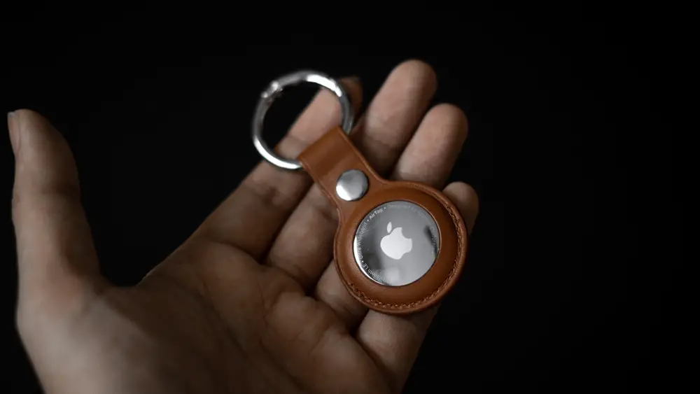 How to Stop an Apple AirTag from Beeping: This photo shows a hand holds an Apple AirTag protected by a leather key ring.