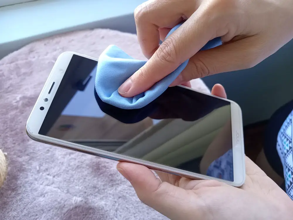 Fix ghost touch issues on Android phones: This photo shows a person wiping the screen of an Android phone with a soft microfiber cloth.