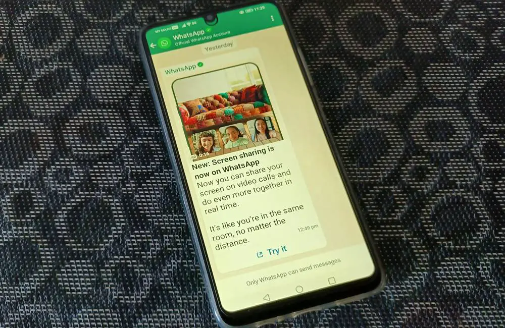 This photo depicts an Android phone with its screen featuring the WhatsApp chat window of the WhatsApp Official Account. The content of the chat showing a video promoting the WhatsApp's Screen Sharing feature.