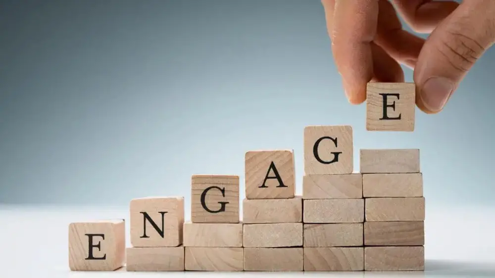 This photo depicts an individual stacking small wooden puzzles that feature the word 'Engage'.