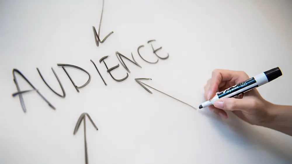 This photo depicts an individual writing the word 'Audience' on a white board with a marker pen.