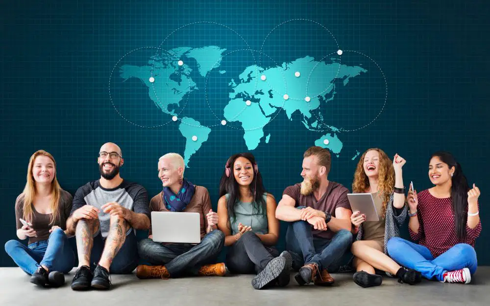 This photo depicts a group of people sitting on the floor, with a world map featured prominently in the background.