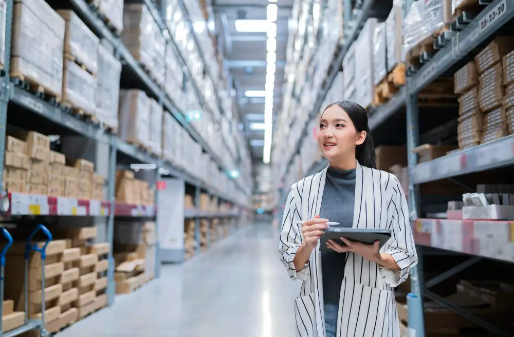 How to Implement Strategic Category Management in Procurement: This photo depicts a female business owner using a digital tablet to check the amount of stock product inventory on shelves at a distribution warehouse.