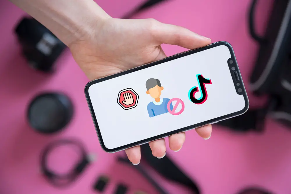 This photo depicts a hand holding a smartphone with its screen featuring a 'Stop' and a 'Blocked Person' icon, along with the TikTok logo.