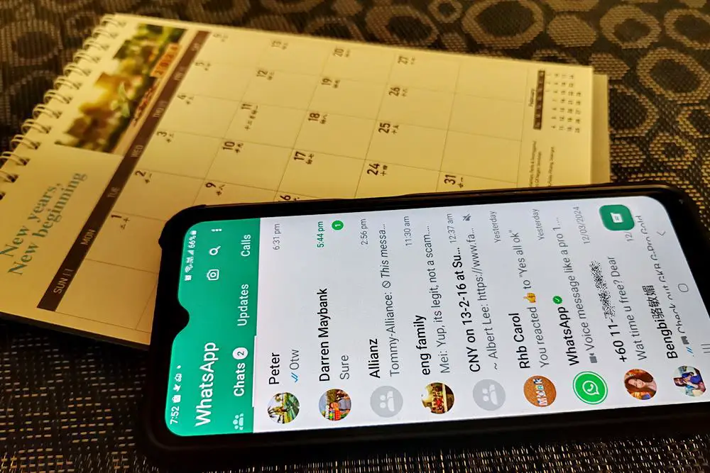 This photo depicts a smartphone with its screen displaying the WhatsApp chats page, placed on top of a table calendar.