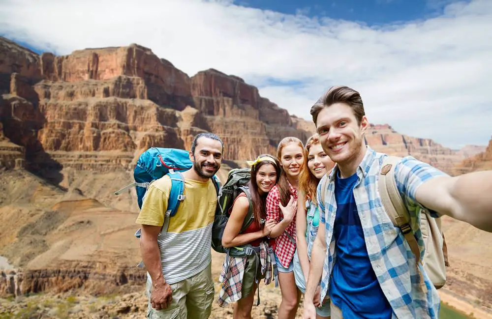 This photo depicts a group of friends or travelers with backpacks taking a 0.5 selfie amidst the rocks of Grand Canyon National Park.