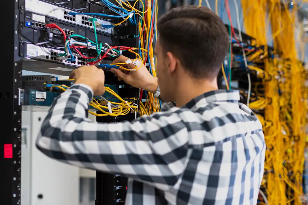 This photo depicts a young man managing and organizing cables and wiring within server racks.