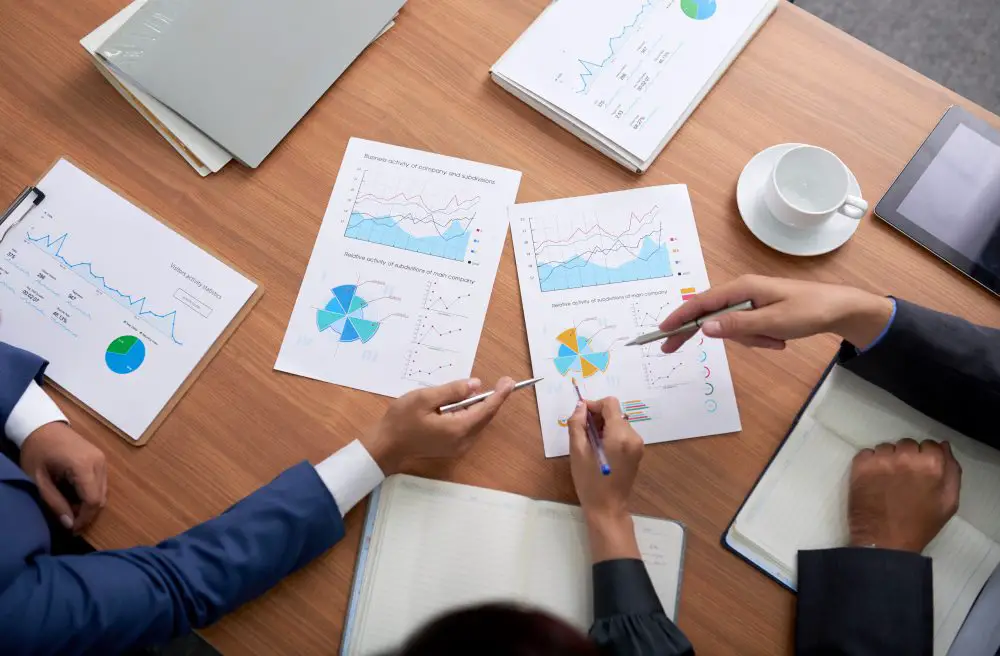 This photo depicts three business professionals sitting at a meeting, examining charts, and reviewing category strategies.