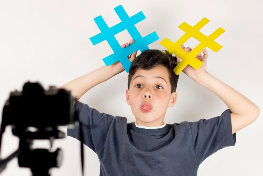 This photo depicts a young social media influencer making a video of himself holding two physical hashtag symbols.