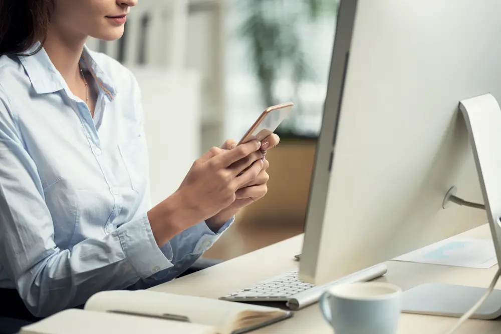 Top 10 Dangerous Emails You Should Never Click On: This photo depicts a woman sitting calmly typing on her smartphone in an office.